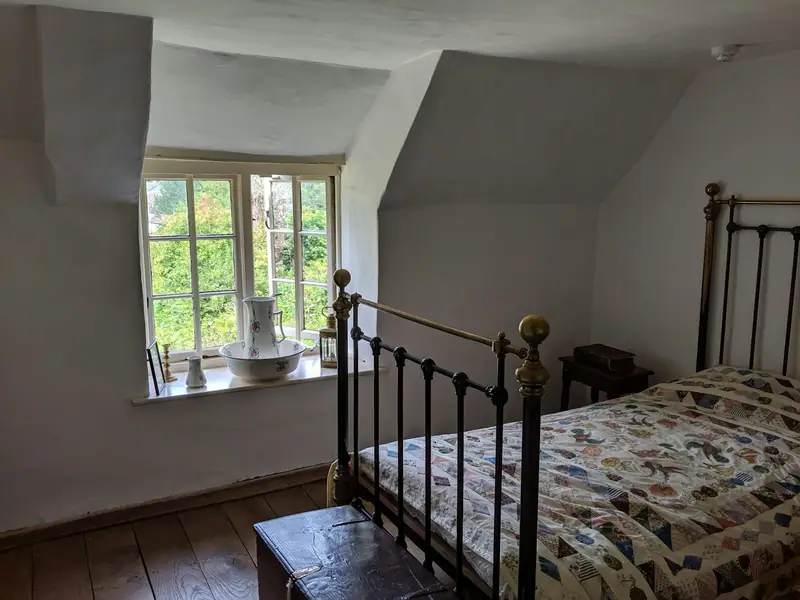 Chambre sous les combles avec lit en fer, couette en patchwork et fenêtre sur la verdure