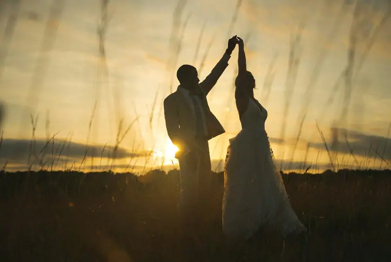 Silhouettes de mariés dansant dans les herbes au soleil couchant