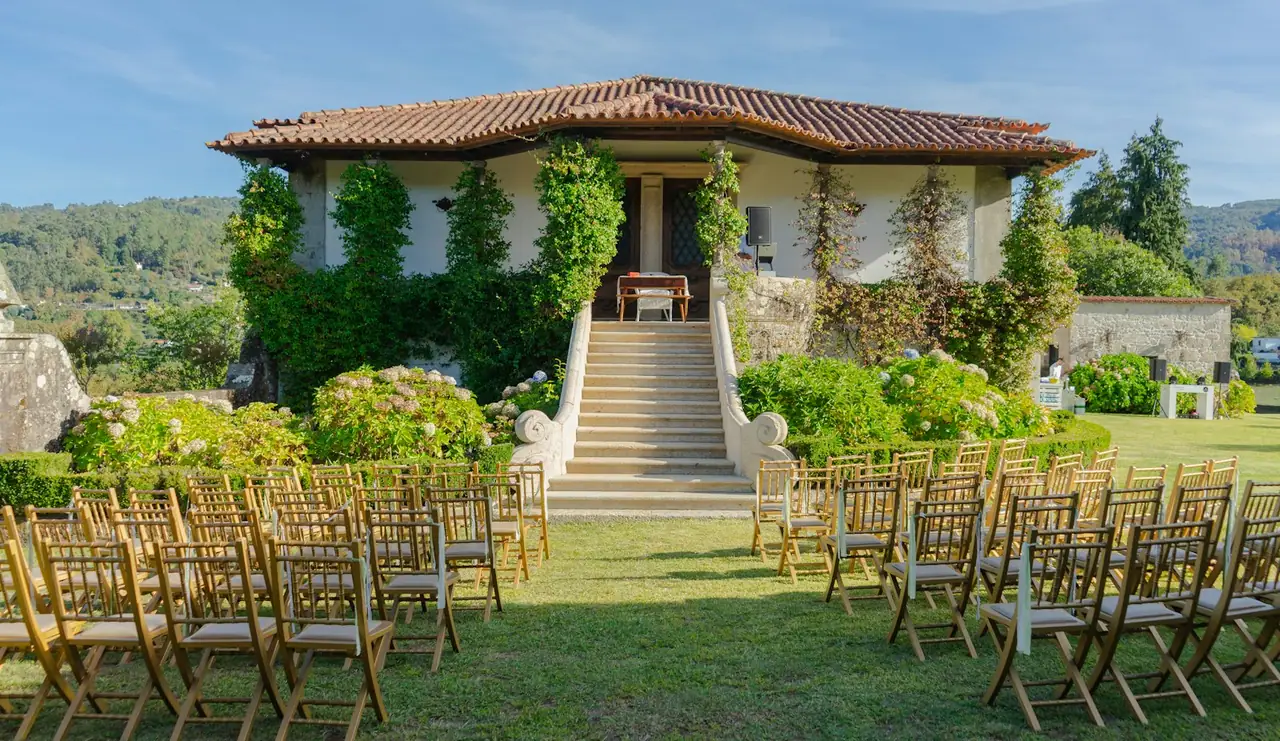 Le logis couvert de tuiles rondes, escalier de pierre et chaises de cérémonie sur la pelouse